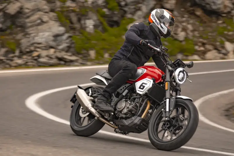 Motocyklista w kasku jedzie czerwonym motocyklem po krętej drodze. Idealny motor na początek przygody z jazdą.