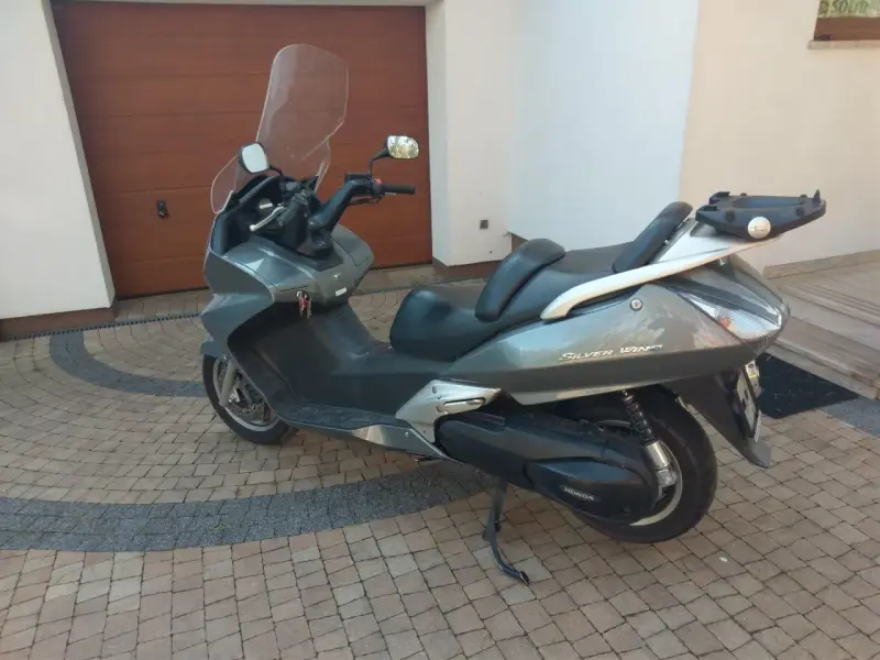 Szary skuter Honda Silver Wing 600 stoi na kostce brukowej przed garażem.